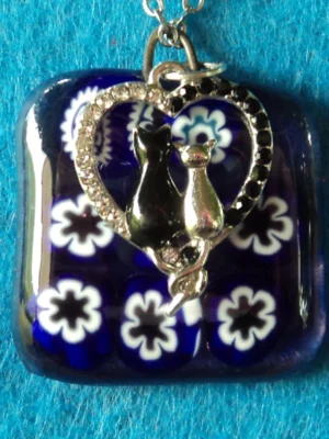 Pendentif en verre mauve semi_transparent avec 9 millefioris blanc et bleu foncé fondus. Une breloque représentant un couple de chat dans un cœur, avec des brillants, a été accrochée.