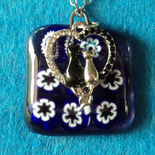 Pendentif en verre mauve semi_transparent avec 9 millefioris blanc et bleu foncé fondus. Une breloque représentant un couple de chat dans un cœur, avec des brillants, a été accrochée.