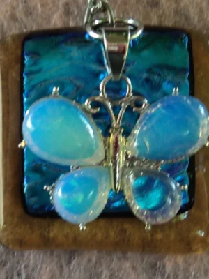 Pendentif carré en verre dichroïque bleu turquoise sur verre orange semi-transparent. Une breloque représentant un papillon en aigue-marine